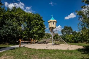 Park przy ul. Pakosławskiej Widok na drewnianą wieżę z metalową zjeżdżalnią i wspinaczką linową.