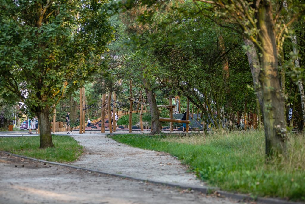 Skwer przy ul. Mikołowskiej- widok na aleję drzew i ścieżkę żwirową, na drugim planie fragment placu zabaw.