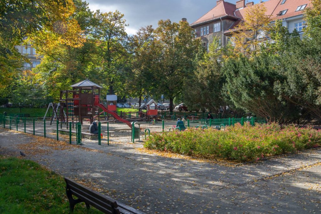 Skwer Ireny Sendlerowej - widok na grupę krzewów i plac zabaw, widoczny domek ze zjeżdżalnią.