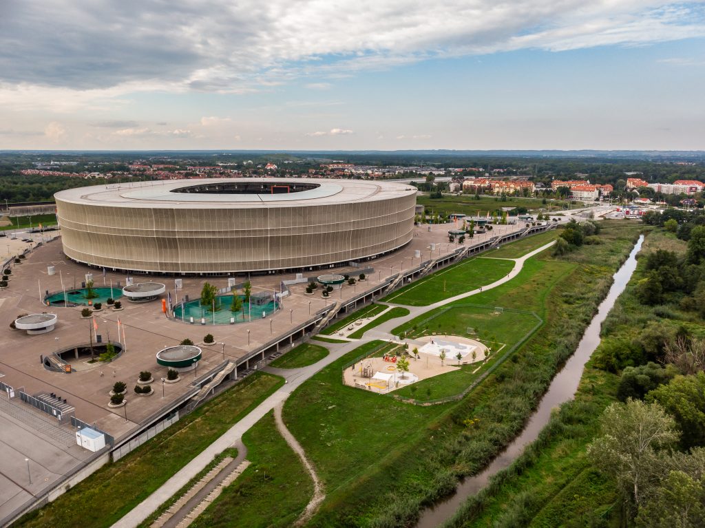 Skwer przy kładce Pilczyckiej-al. Śląskiej-widok na plac zabaw, Stadion i otaczającą roślinność, z tyłu widoczna zabudowa.