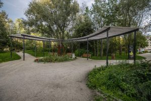 Park Leonarda da Vinci- widok na rabatę bylinową, w środku rzeźba Człowieka witruwiańskiego, za nią półokrągła pergola i ławki z oparciem.