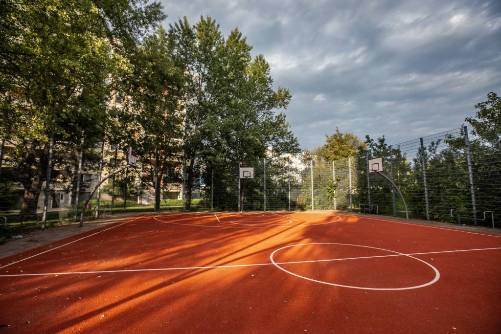 Skwer ks. Leszka Jabłońskiego- widok na boisko sportowe do koszykówki (wewnątrz znajdują się trzy kosze do gry i kilka ławek) oraz otaczające je zadrzewienie.