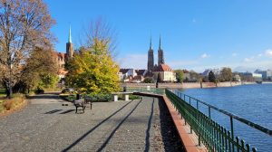 Bulwar Piotra Włostowica - ujęcie na bulwar, na pierwszym planie ławka oraz Pomnik Odry, na drugim planie nasadzenia bylin, okazy drzew i krzewów, w tle rzeka i zabudowa miasta.