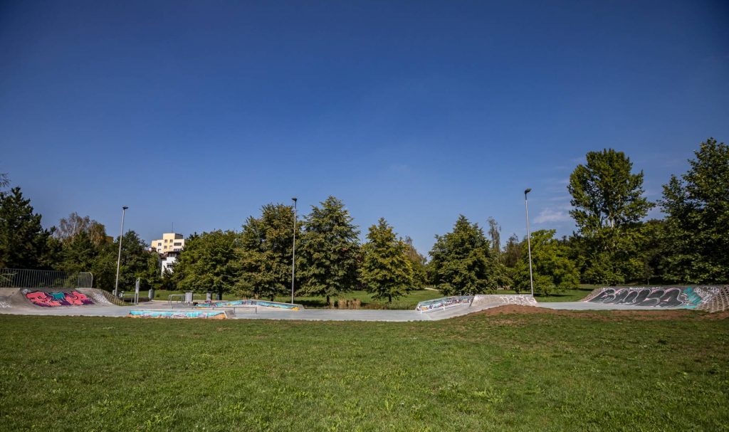 Park przy ul. Canaletta - widok na betonowy skate park, na drugim planie szpaler drzew.