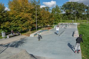 Park przy ul. Canaletta - zbliżone ujęcie na skate park, widoczne bawiące się dzieci, po lewej stronie szpaler drzew.