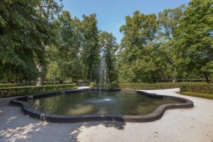 Park Brochowski- widok na fontannę, za nią żywopłoty i zadrzewienie.