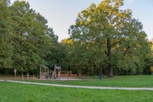 Park Złotnicki- ujęcie na drewniany plac zabaw, widoczne drewniane domki, zjeżdżalnia i hamak.